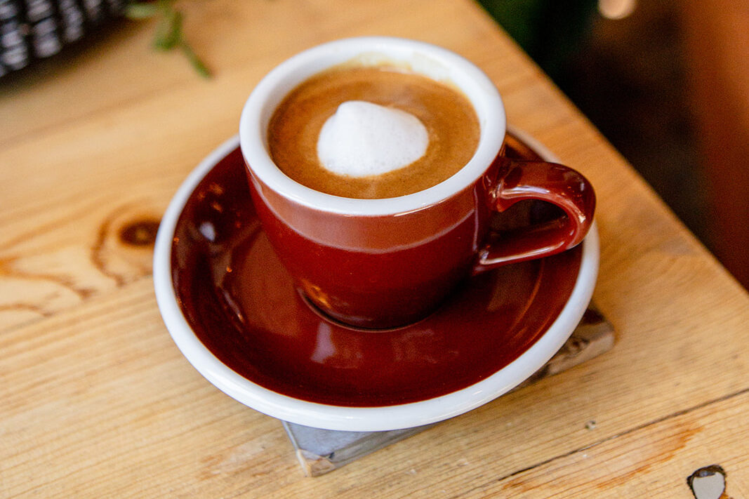 A hot coffee in a cup with matching saucer on a light wood table.