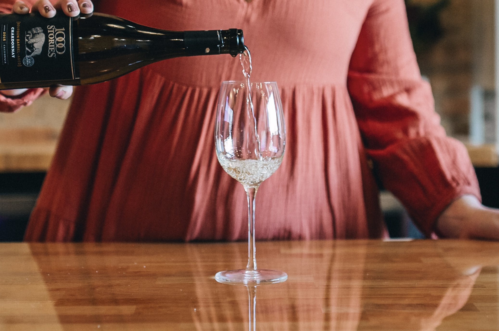 Image of wine being poured from a bottle into a glass in front of a woman.
