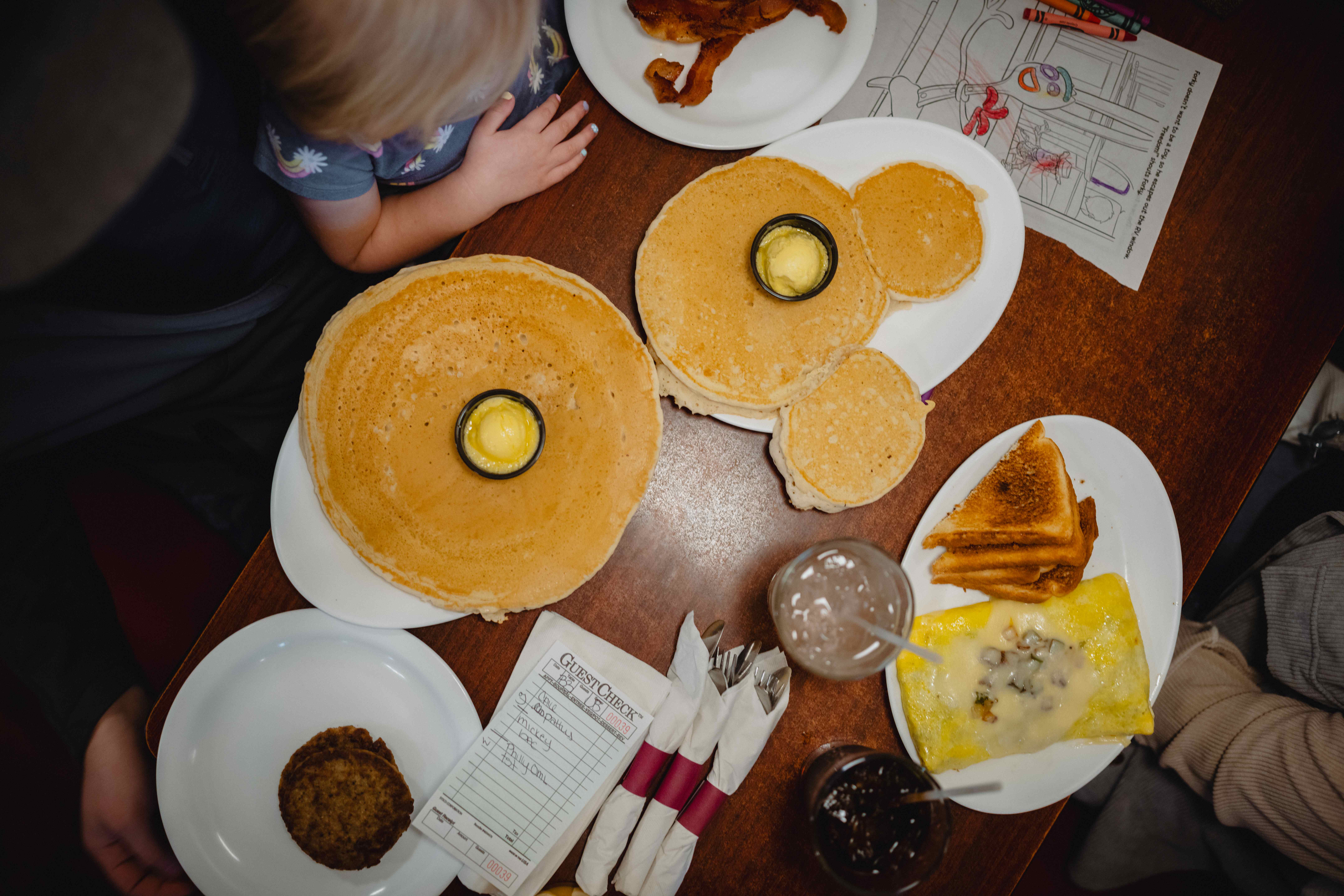 An image of a table at Cook's Kitchen in Brookings, SD covered with plates filled with pancakes, eggs, toast, sausage and bacon. The table is surrounded by a family.