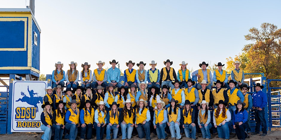 A large group photo of SDSU rodeo athletes in front of a sign that reads "SDSU Rodeo"