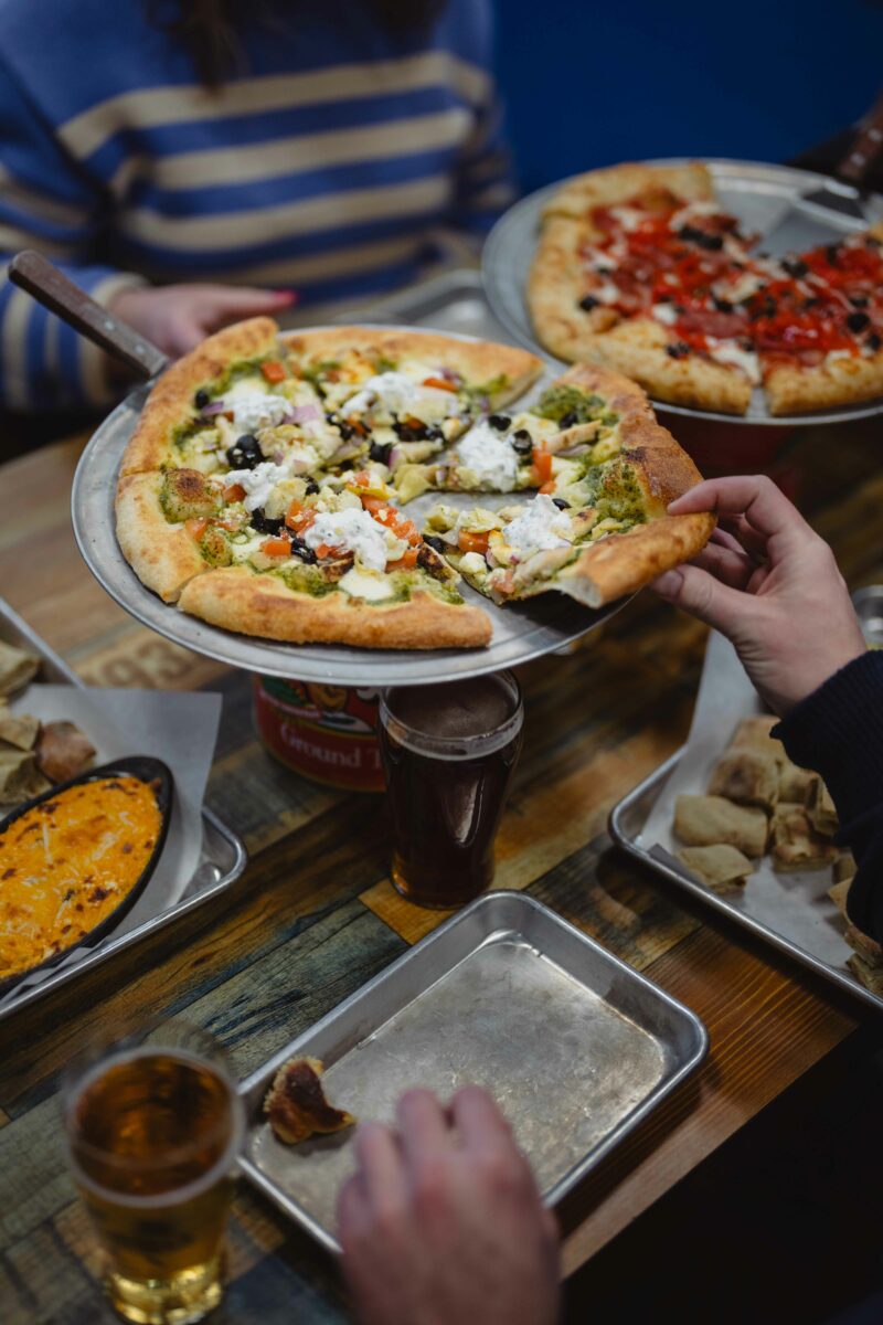 table with pizzas, drinks and sides surrounded by two guests.