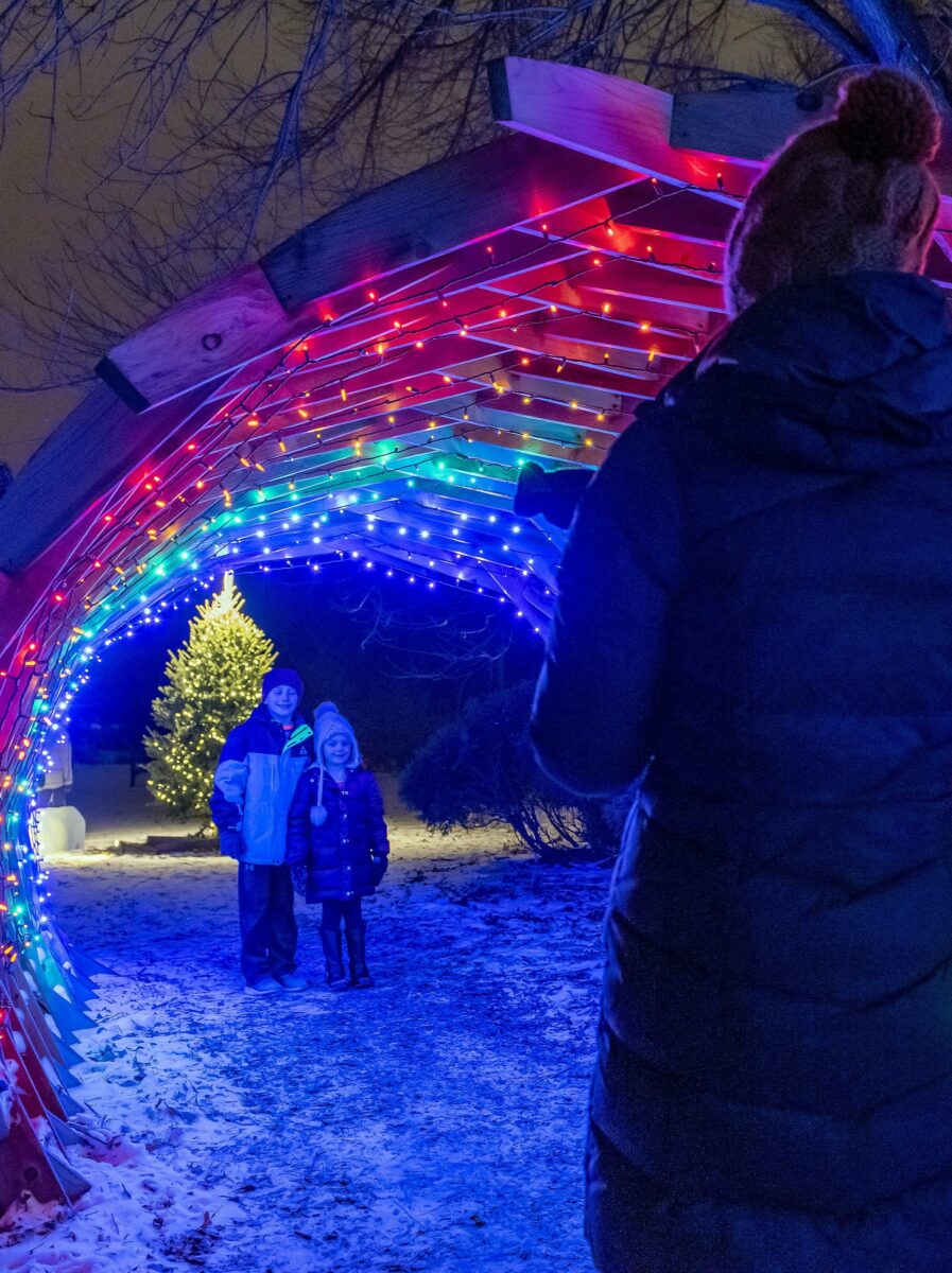 a parent taking a photo of two children under a tunnel of Christmas lights at Garden Glow in Brookings