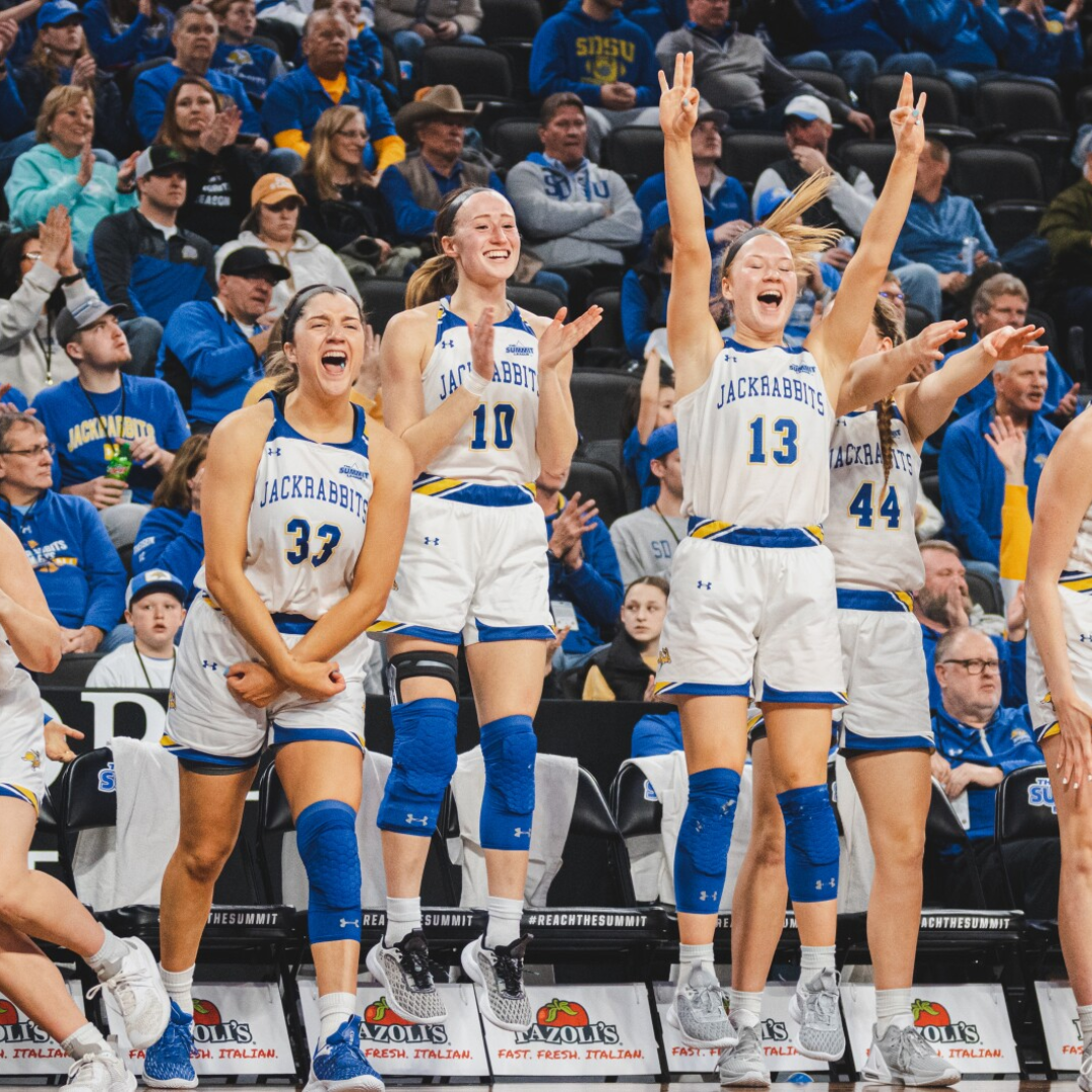 SDSU women's basketball team jumping and cheer near the team's bench.