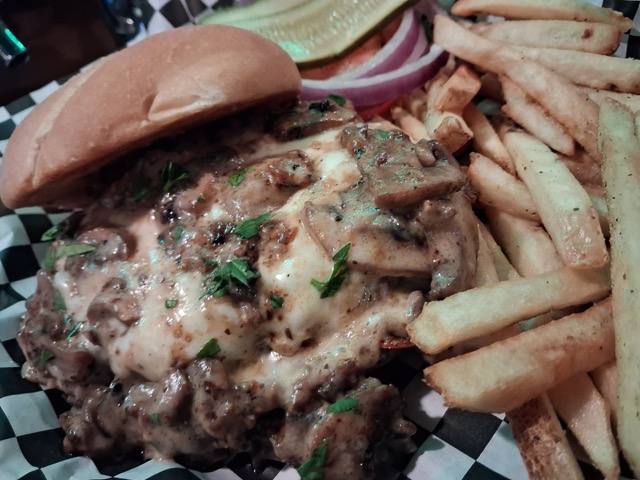 A burger with a cheesy mushroom sauce served on a bun with a side of fries