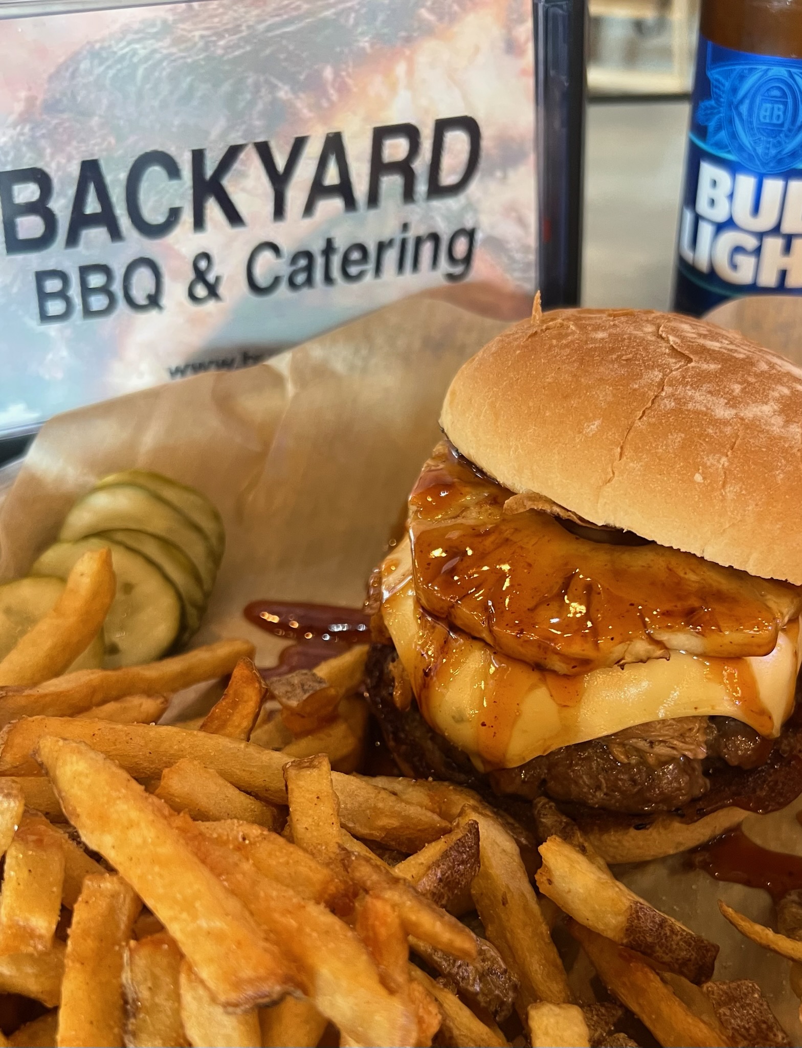 Burger with a slice of pineapple and a side of fries and pickles from Backyard BBQ