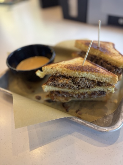 Two half's of a burger served on toasted bread with a side of sauce