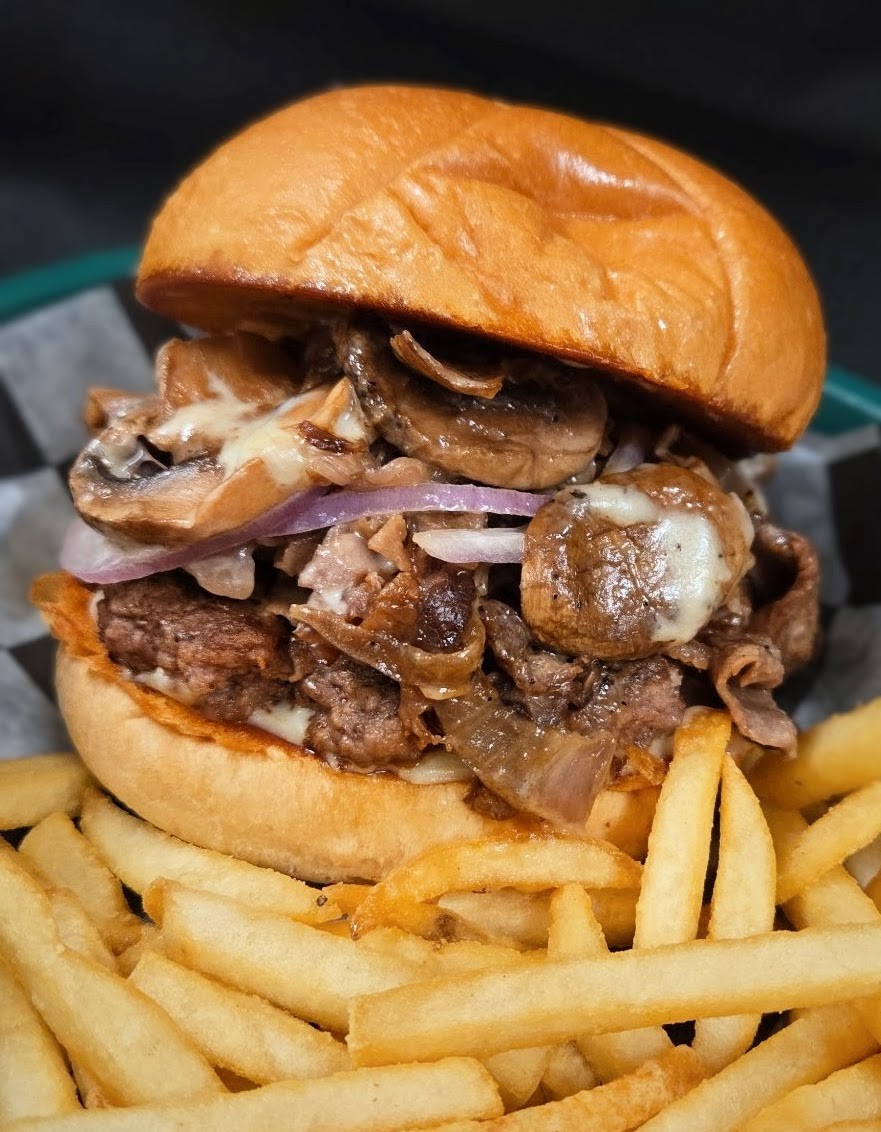 A burger topped with sauteed mushrooms served with a side of fries