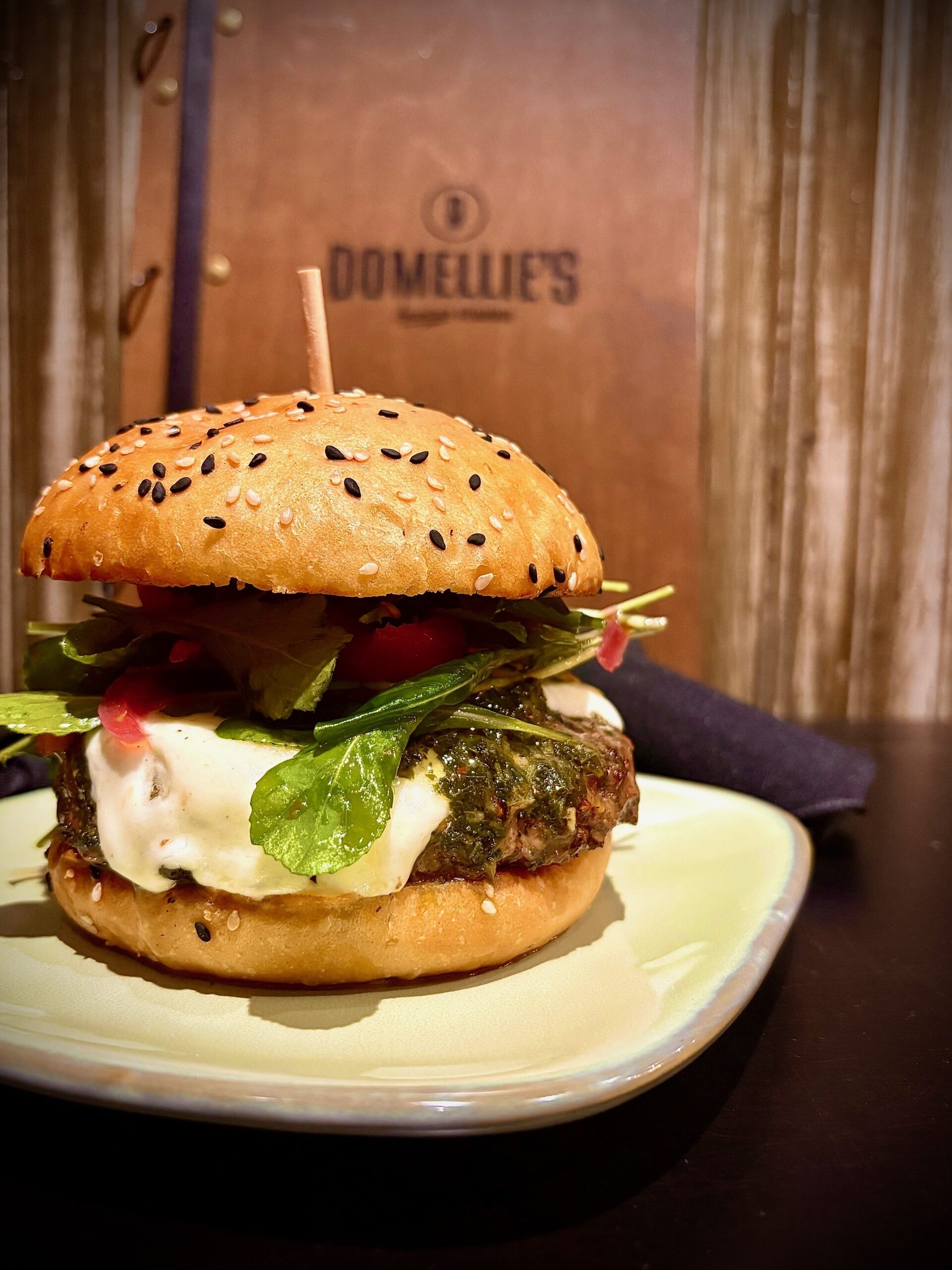 Burger with green and chimchurri sauce on top of a golden bun with everything bagel seasoning