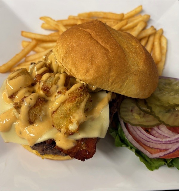 A burger topped with cheese curds and a aioli sauce with a side of fries