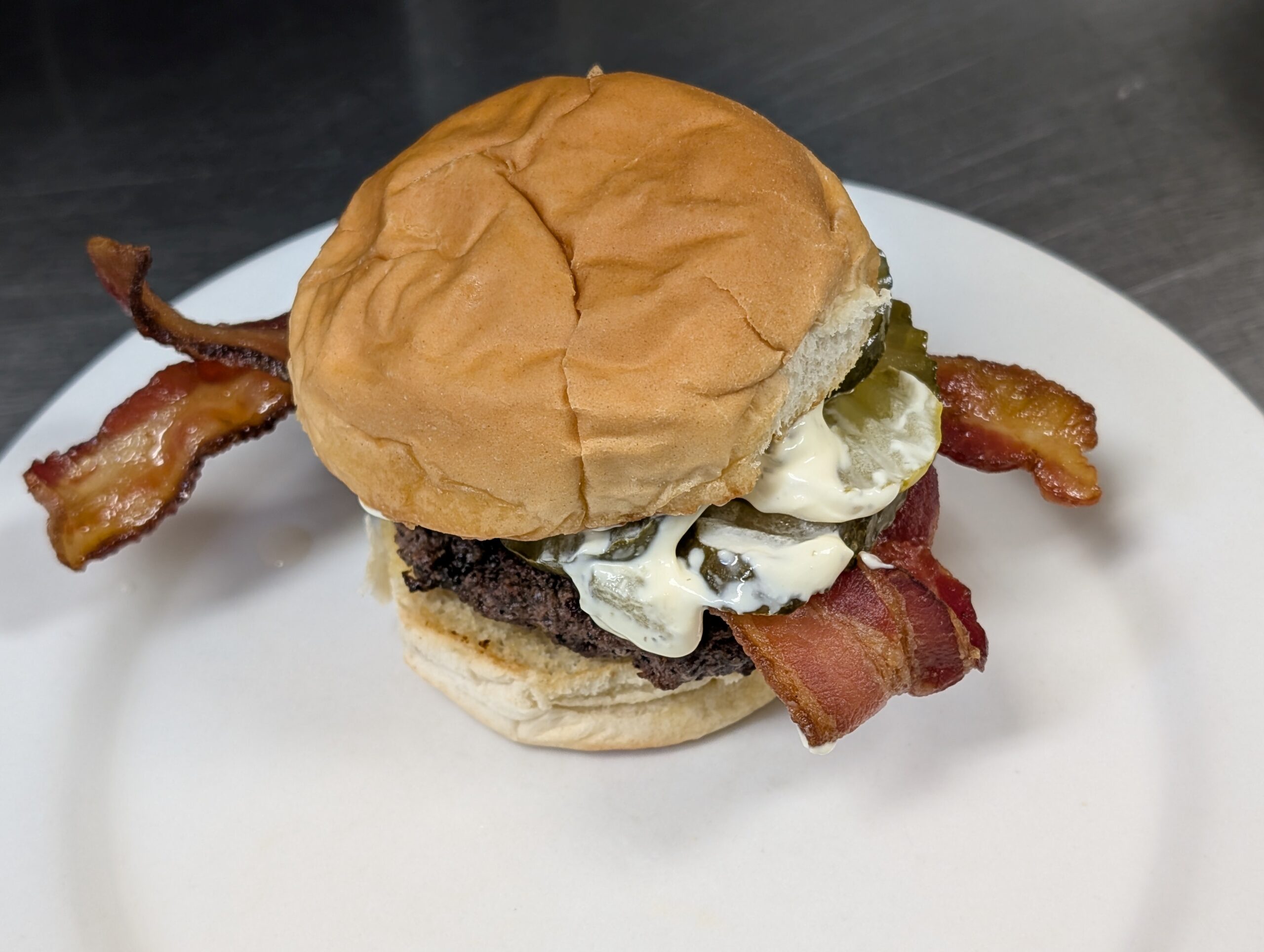 A burger with bacon slices and pickles with a white sauce