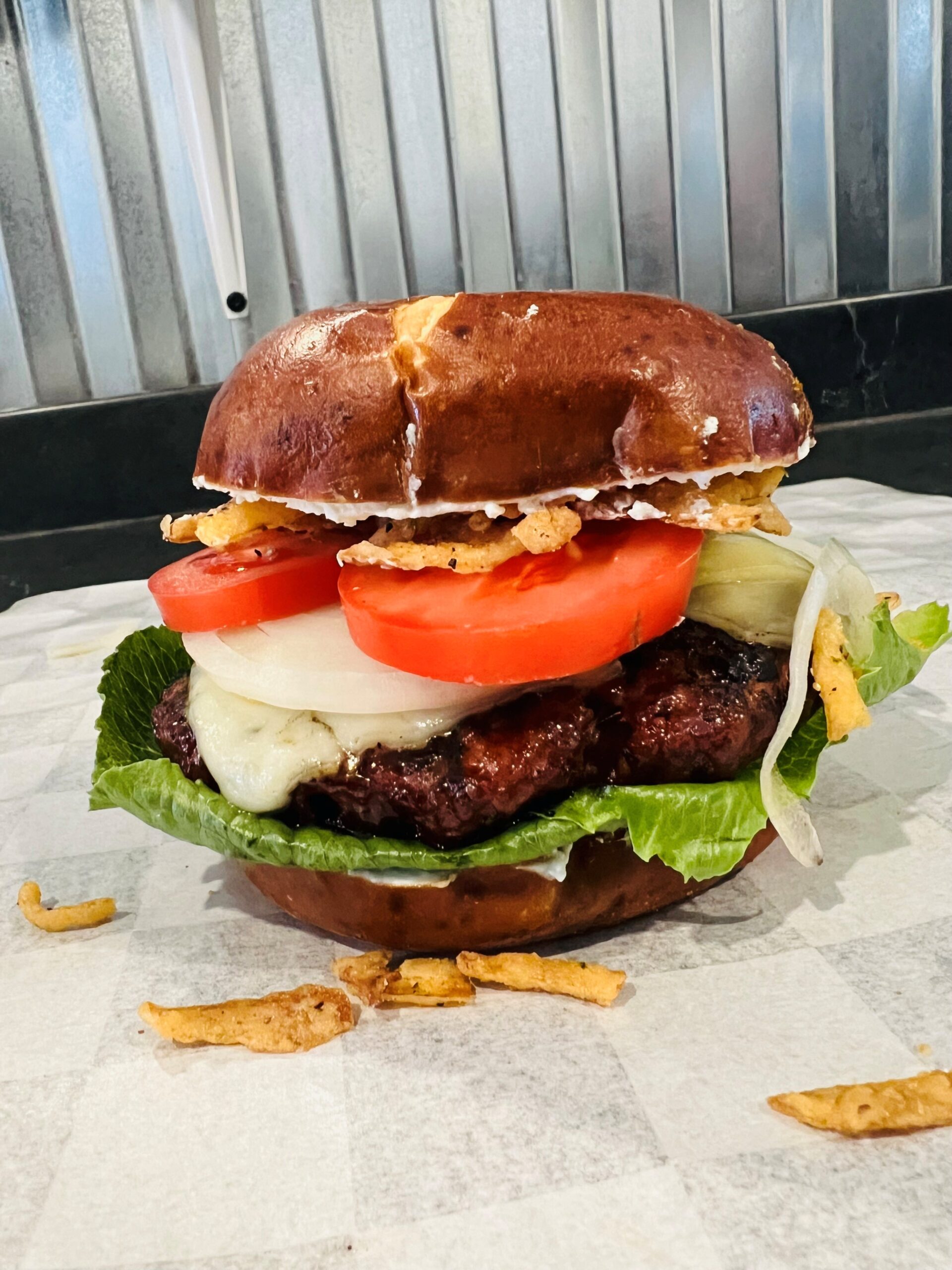 A burger on a pretzel bun with tomatoes and crunchy onions