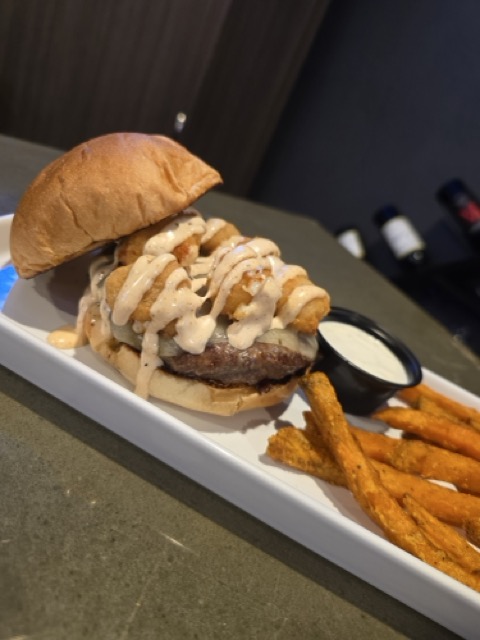 Burger toped with cheese curds and a sauce served with a side of fries