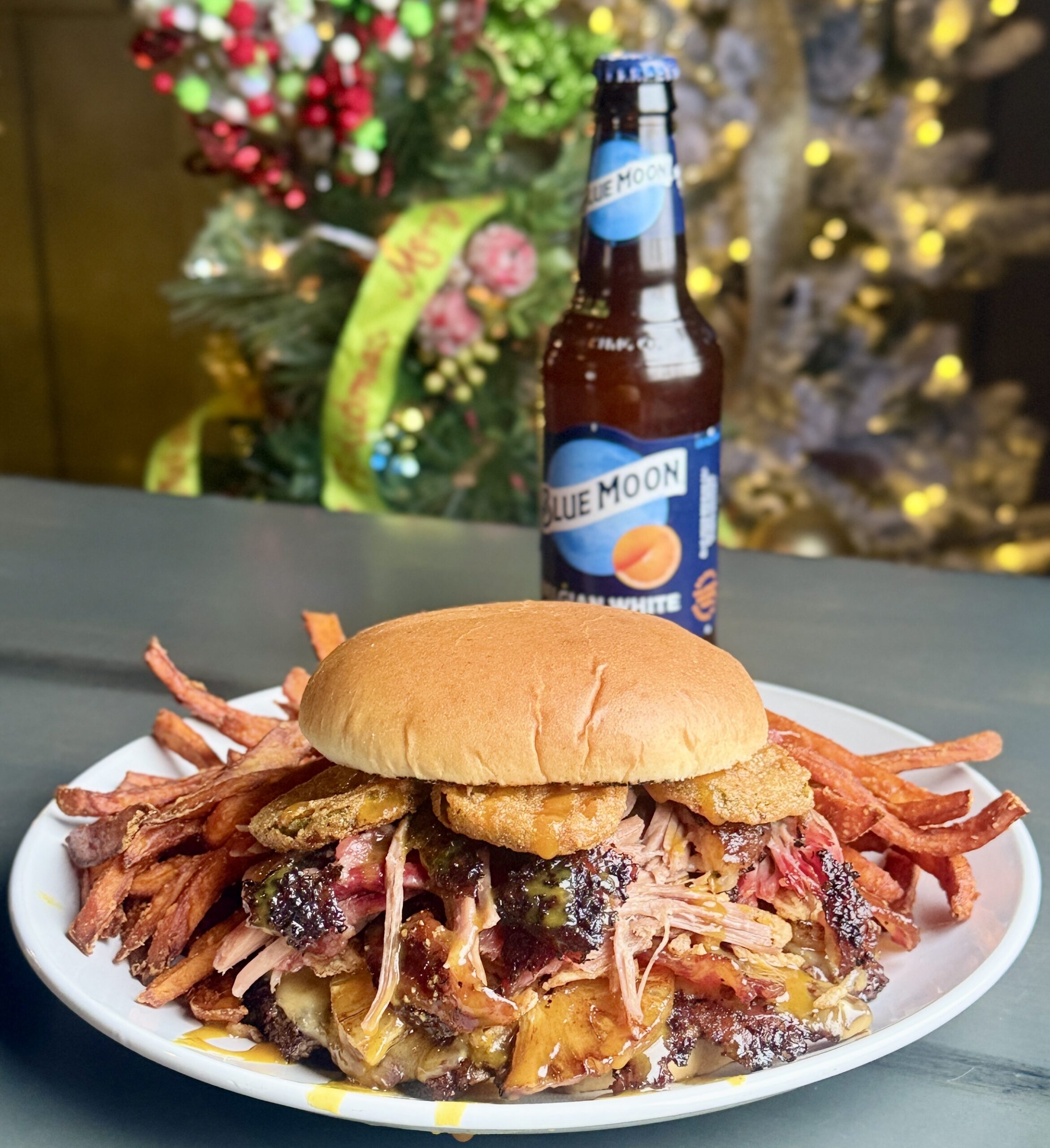 Burger with bacon slices, fried pickles and lots of other toppings. with a side of potato fries and a drink